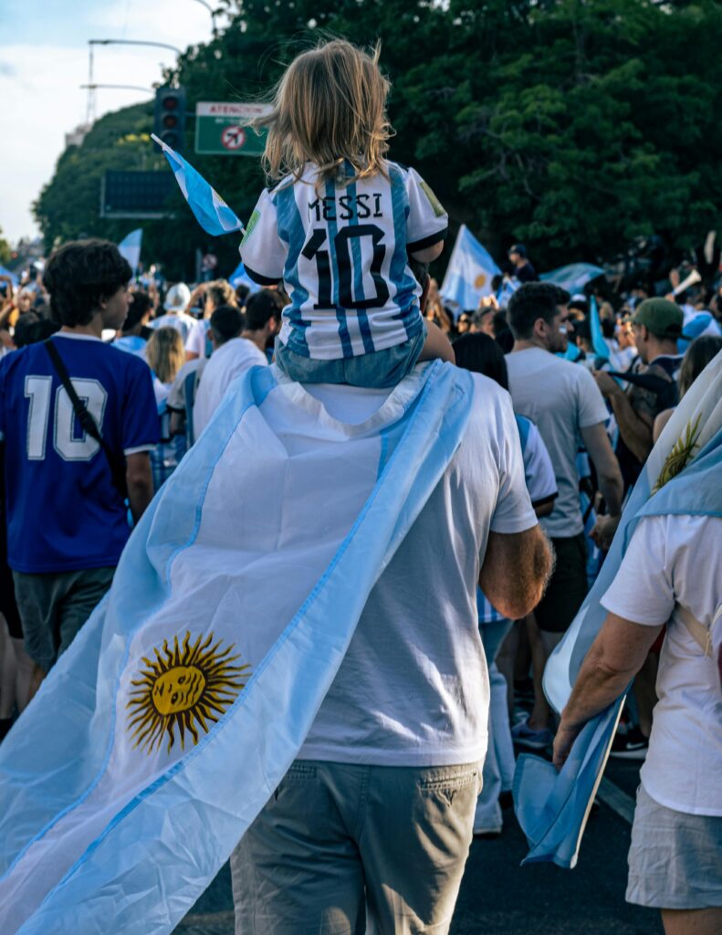 Father carries child in Messi jersey during a Buenos Aires football celebration, showcasing Argentinian pride.