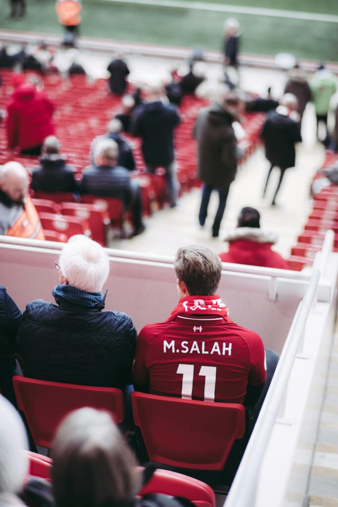 Fans in red jerseys sit in a stadium, showcasing football spirit with vibrant energy.