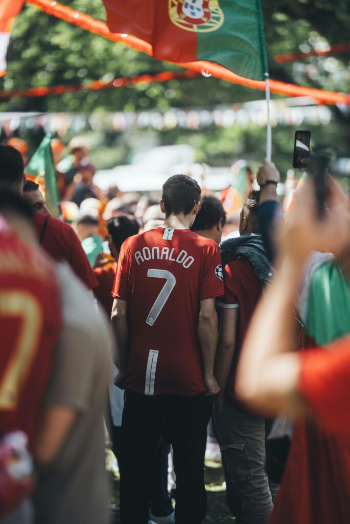 A vibrant outdoor scene of enthusiastic soccer fans wearing jerseys and waving flags during a celebration.